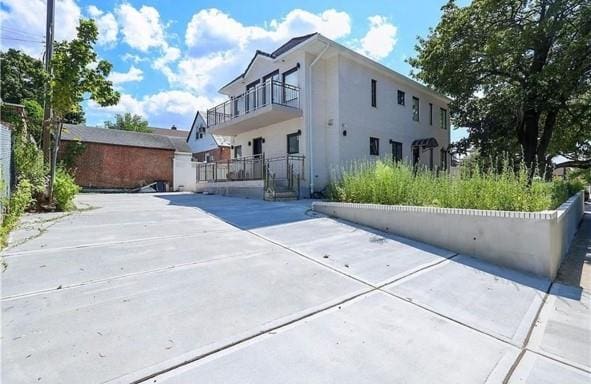 back of property featuring a balcony, stucco siding, and fence