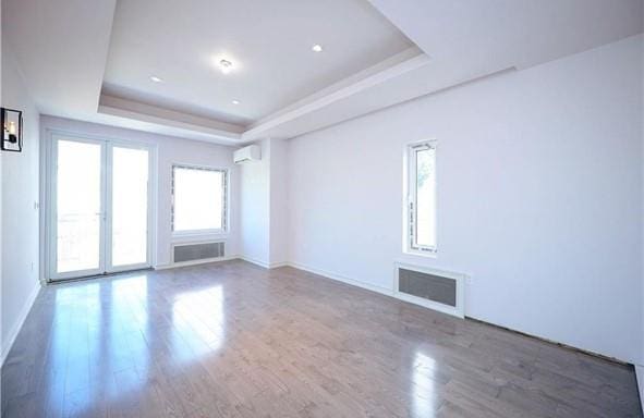 spare room with a tray ceiling, a wall mounted AC, wood finished floors, baseboards, and visible vents