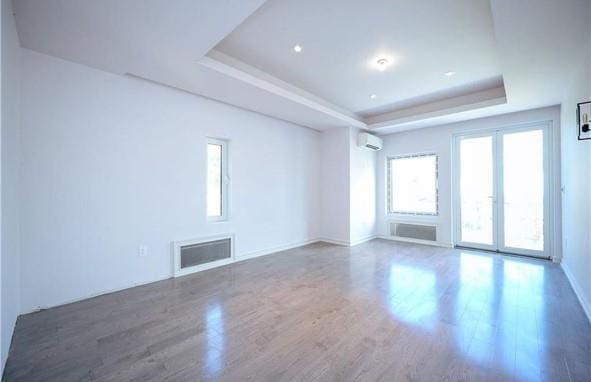 empty room featuring visible vents, baseboards, wood finished floors, a raised ceiling, and a wall unit AC