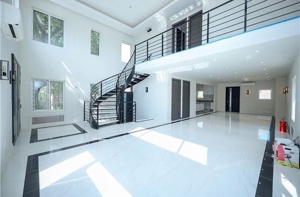 interior space featuring a wall mounted air conditioner, stairs, a towering ceiling, and marble finish floor