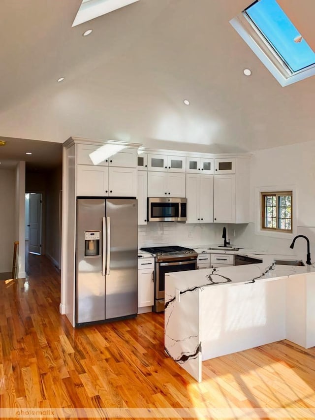 kitchen featuring sink, stainless steel appliances, kitchen peninsula, light hardwood / wood-style floors, and white cabinets