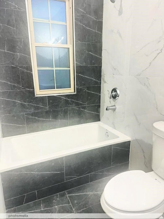 bathroom featuring tile walls, tiled shower / bath combo, and toilet