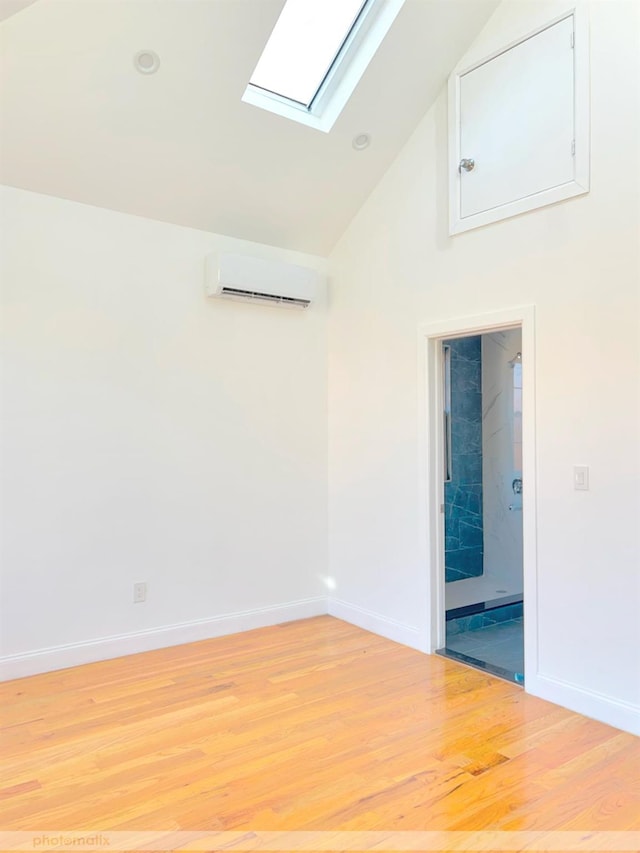 empty room with high vaulted ceiling, a skylight, light hardwood / wood-style flooring, and a wall mounted AC