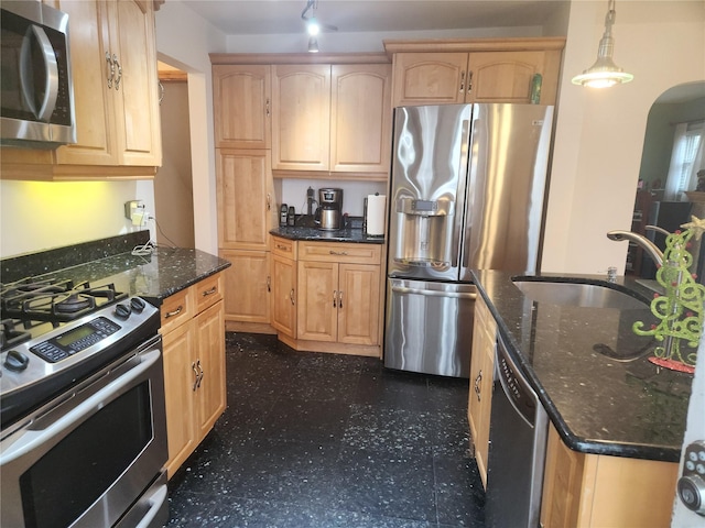 kitchen with appliances with stainless steel finishes, dark stone counters, sink, light brown cabinets, and decorative light fixtures