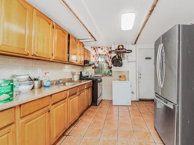 kitchen featuring decorative backsplash, stainless steel fridge, black range with gas stovetop, sink, and light tile patterned floors