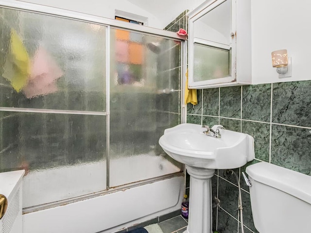 bathroom with tile patterned floors, toilet, enclosed tub / shower combo, and tile walls