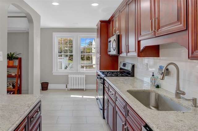 kitchen with light stone countertops, decorative backsplash, appliances with stainless steel finishes, sink, and radiator heating unit