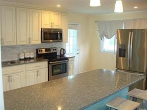 kitchen featuring white cabinetry, a center island, stainless steel appliances, backsplash, and dark stone countertops