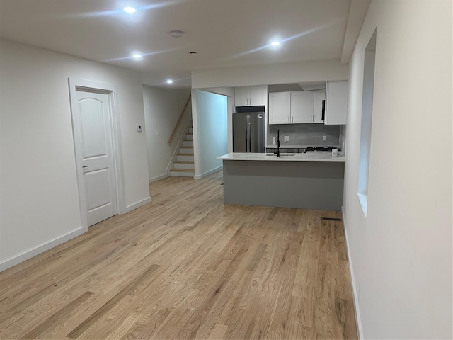 kitchen with kitchen peninsula, decorative backsplash, light wood-type flooring, white cabinetry, and stainless steel refrigerator