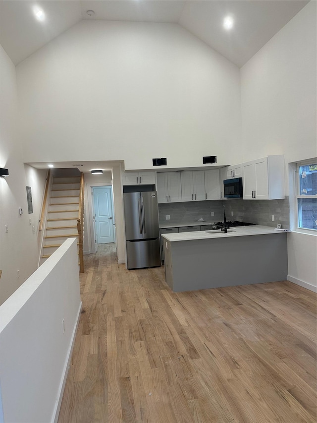 kitchen featuring light hardwood / wood-style floors, stainless steel fridge, kitchen peninsula, and high vaulted ceiling