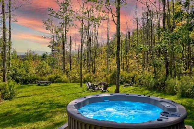 pool at dusk featuring a hot tub and a lawn