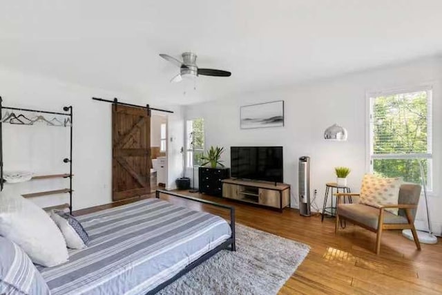 bedroom with a barn door, ceiling fan, and hardwood / wood-style flooring