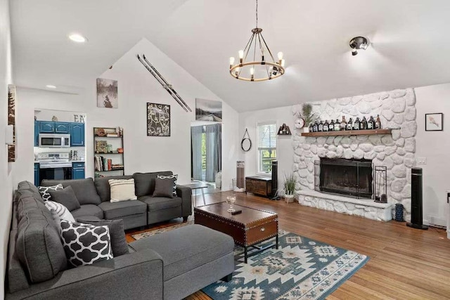 living room with vaulted ceiling, a stone fireplace, light wood-type flooring, and a chandelier