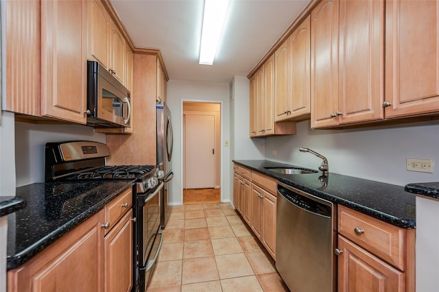 kitchen featuring light tile patterned floors, stainless steel appliances, dark stone counters, and sink