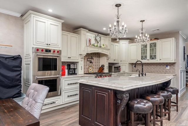 kitchen featuring sink, stainless steel double oven, light stone counters, decorative light fixtures, and a breakfast bar