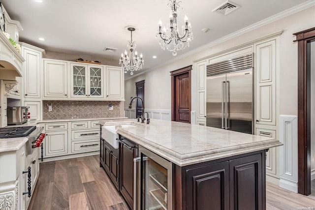 kitchen with sink, an island with sink, appliances with stainless steel finishes, wood-type flooring, and beverage cooler