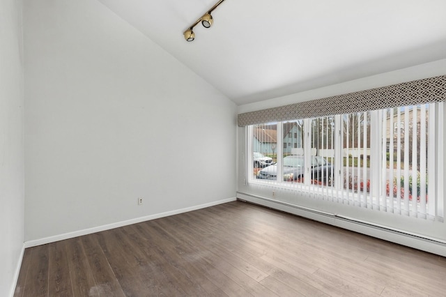 spare room featuring rail lighting, hardwood / wood-style flooring, vaulted ceiling, and a baseboard heating unit