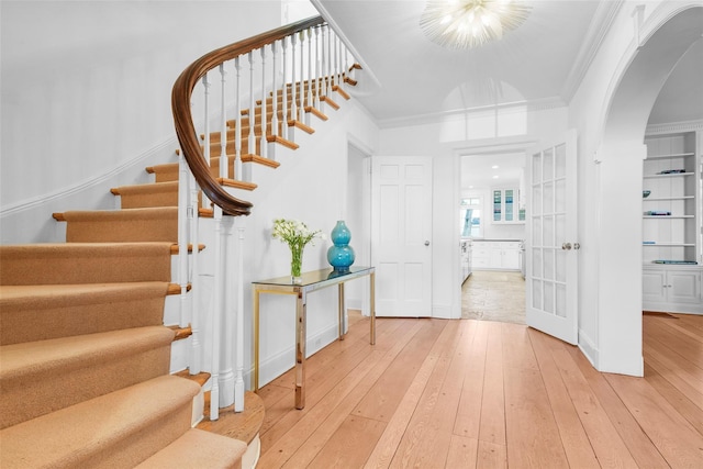 entryway with light wood-style floors, arched walkways, ornamental molding, and stairway