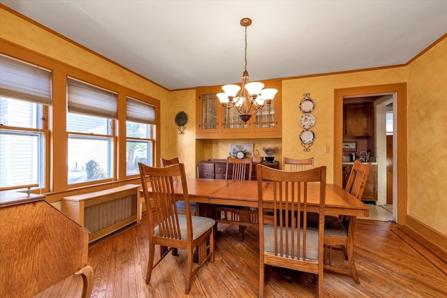 dining room with hardwood / wood-style floors, an inviting chandelier, radiator, and ornamental molding