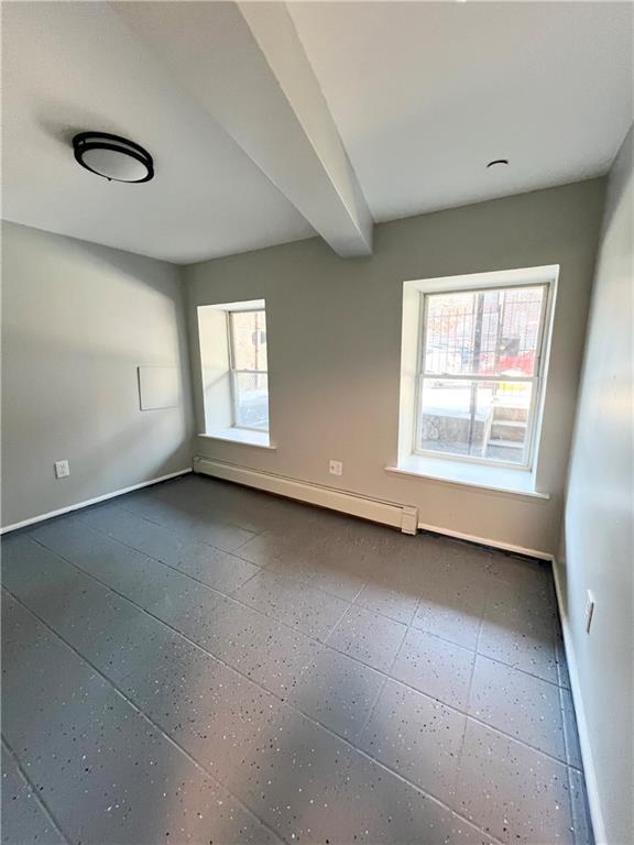 unfurnished room with beamed ceiling, a baseboard heating unit, and a healthy amount of sunlight