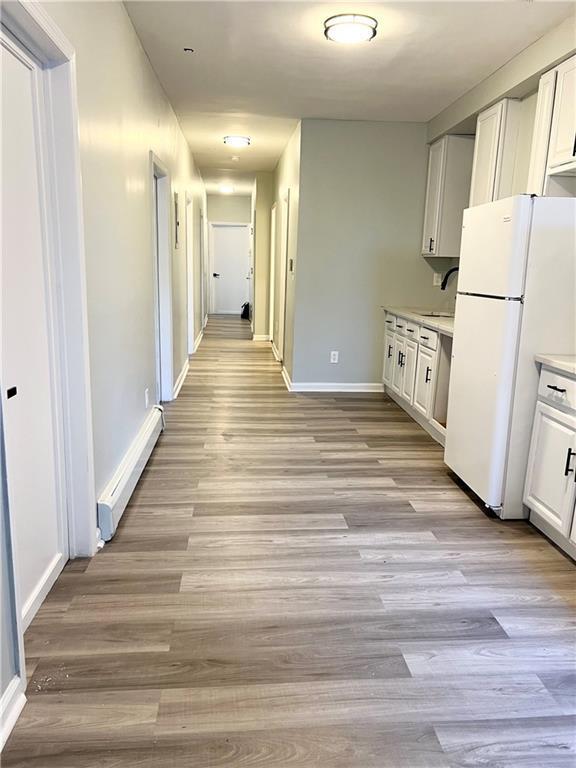 kitchen featuring white cabinetry, sink, white refrigerator, a baseboard heating unit, and light wood-type flooring