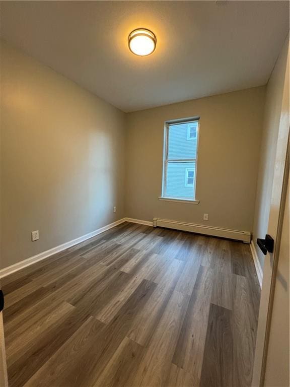 empty room featuring baseboard heating and dark wood-type flooring