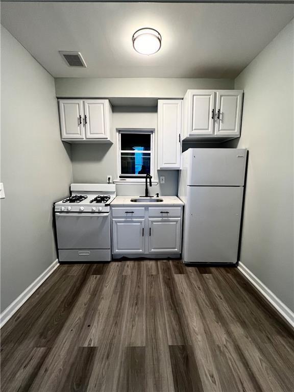 kitchen with sink, dark wood-type flooring, gas range oven, white refrigerator, and white cabinets