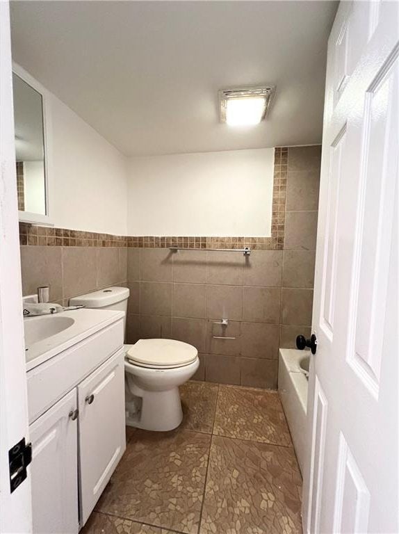 bathroom featuring tile patterned flooring, vanity, toilet, and tile walls