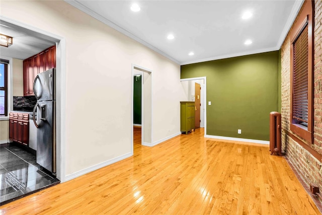 spare room featuring light wood-type flooring, radiator heating unit, brick wall, and ornamental molding