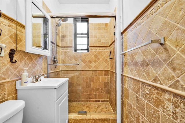 bathroom featuring vanity, toilet, tiled shower, and tile walls