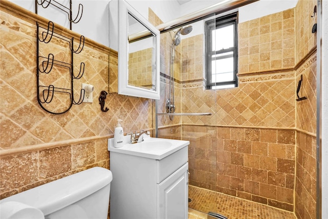 bathroom with a tile shower, vanity, toilet, and tile walls