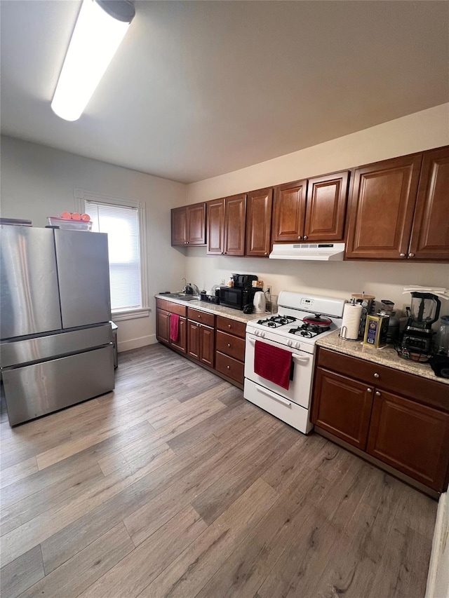 kitchen with white range with gas cooktop, stainless steel fridge, light hardwood / wood-style flooring, and sink