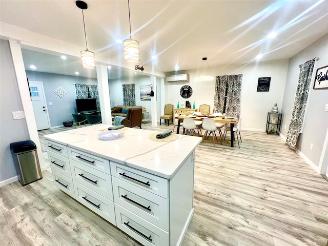 kitchen featuring light wood-type flooring, light stone counters, a wall mounted AC, decorative light fixtures, and a kitchen island