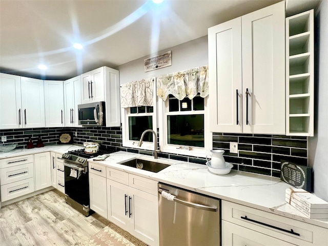 kitchen with light wood-type flooring, backsplash, light stone counters, stainless steel appliances, and sink