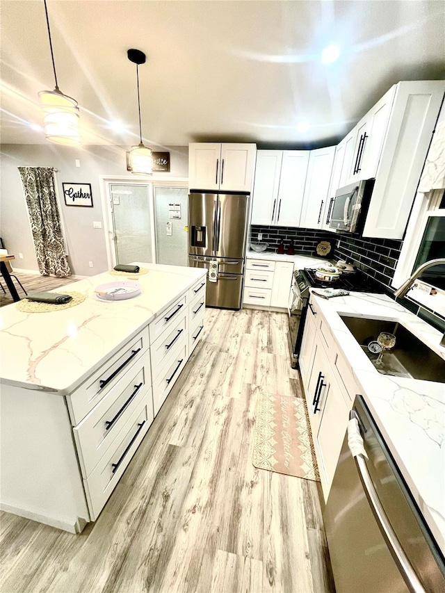 kitchen with light stone countertops, white cabinetry, sink, stainless steel appliances, and decorative light fixtures