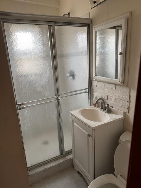 bathroom featuring tile patterned flooring, vanity, toilet, and a shower with door