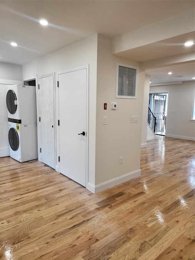 clothes washing area featuring light wood-type flooring and stacked washer and clothes dryer