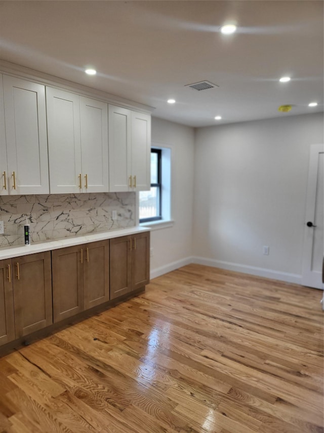 kitchen with white cabinets, light hardwood / wood-style floors, and backsplash