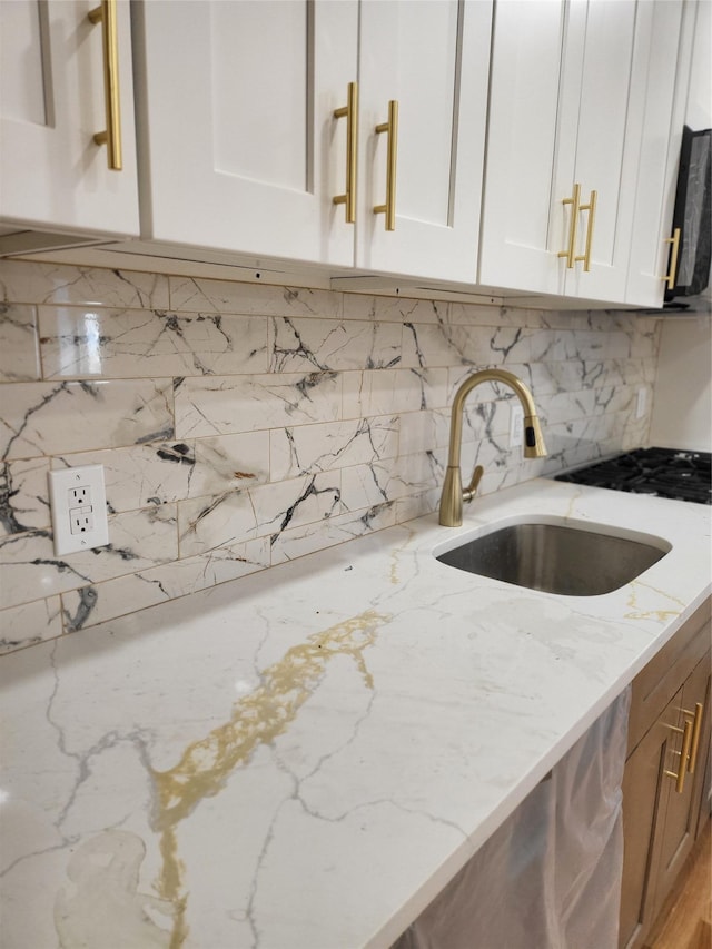 kitchen featuring light stone counters, white cabinetry, and sink