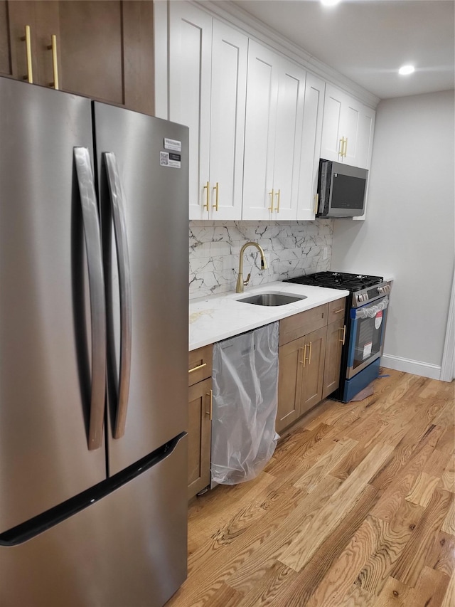 kitchen with backsplash, sink, light wood-type flooring, white cabinetry, and stainless steel appliances