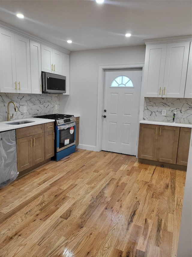 kitchen with tasteful backsplash, stainless steel appliances, sink, white cabinets, and light hardwood / wood-style floors