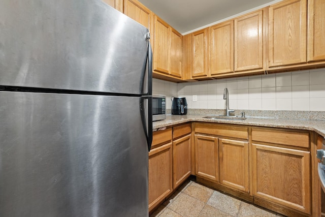 kitchen with backsplash, light stone countertops, sink, and stainless steel appliances