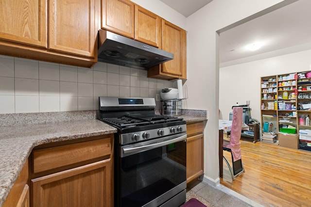 kitchen with tasteful backsplash, light stone counters, stainless steel range with gas stovetop, exhaust hood, and light wood-type flooring