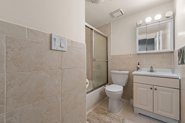 full bathroom with vanity, bath / shower combo with glass door, tile patterned flooring, toilet, and tile walls