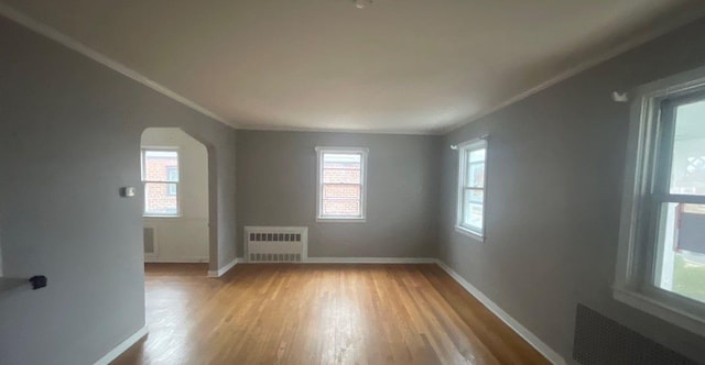 empty room with light wood-type flooring, radiator, and crown molding