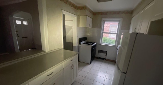 kitchen with light tile patterned floors, white appliances, white cabinetry, and radiator