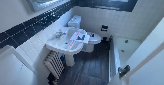 bathroom with radiator, sink, toilet, tile walls, and a tub