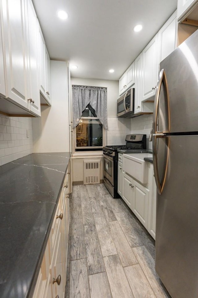 kitchen featuring backsplash, white cabinetry, stainless steel appliances, and light wood-type flooring