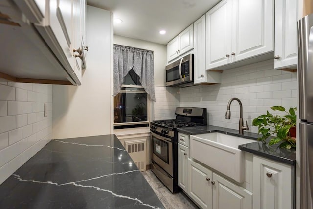 kitchen featuring decorative backsplash, appliances with stainless steel finishes, sink, dark stone countertops, and white cabinets