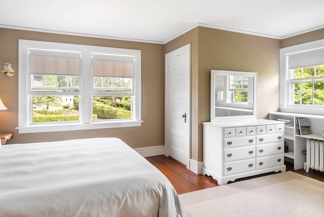 bedroom with hardwood / wood-style floors, radiator heating unit, ornamental molding, and multiple windows